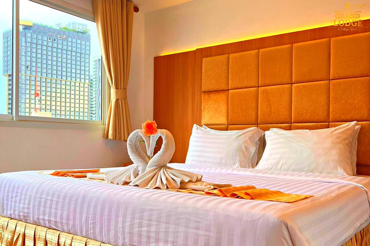 Quarto de hotel com uma cama grande, cabeceira de madeira e uma janela com cortinas.