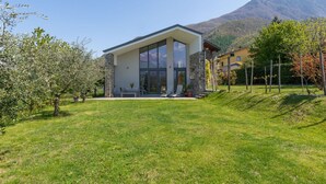 A modern house with a large glass window, a stone exterior, and a mountain backdrop. - Nice apartment in villa for 6 people with WIFI and terrace (Colico)