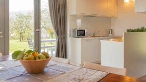 A modern kitchen with white cabinets, a microwave, and a sink. There is a dining table with a bowl of fruit and a patterned table runner. - Nice apartment in villa for 6 people with WIFI and terrace (Colico)