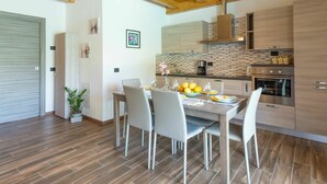 A modern kitchen with wooden beams, a dining area with a table set for four, and a large oven. - Lovely apartment in villa for 5 guests with pool, WIFI, TV and terrace (Colico)