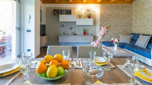 A dining area with a wooden table set for a meal, a bowl of fruit, and a blue sofa in the background. - Lovely apartment in villa for 5 guests with pool, WIFI, TV and terrace (Colico)