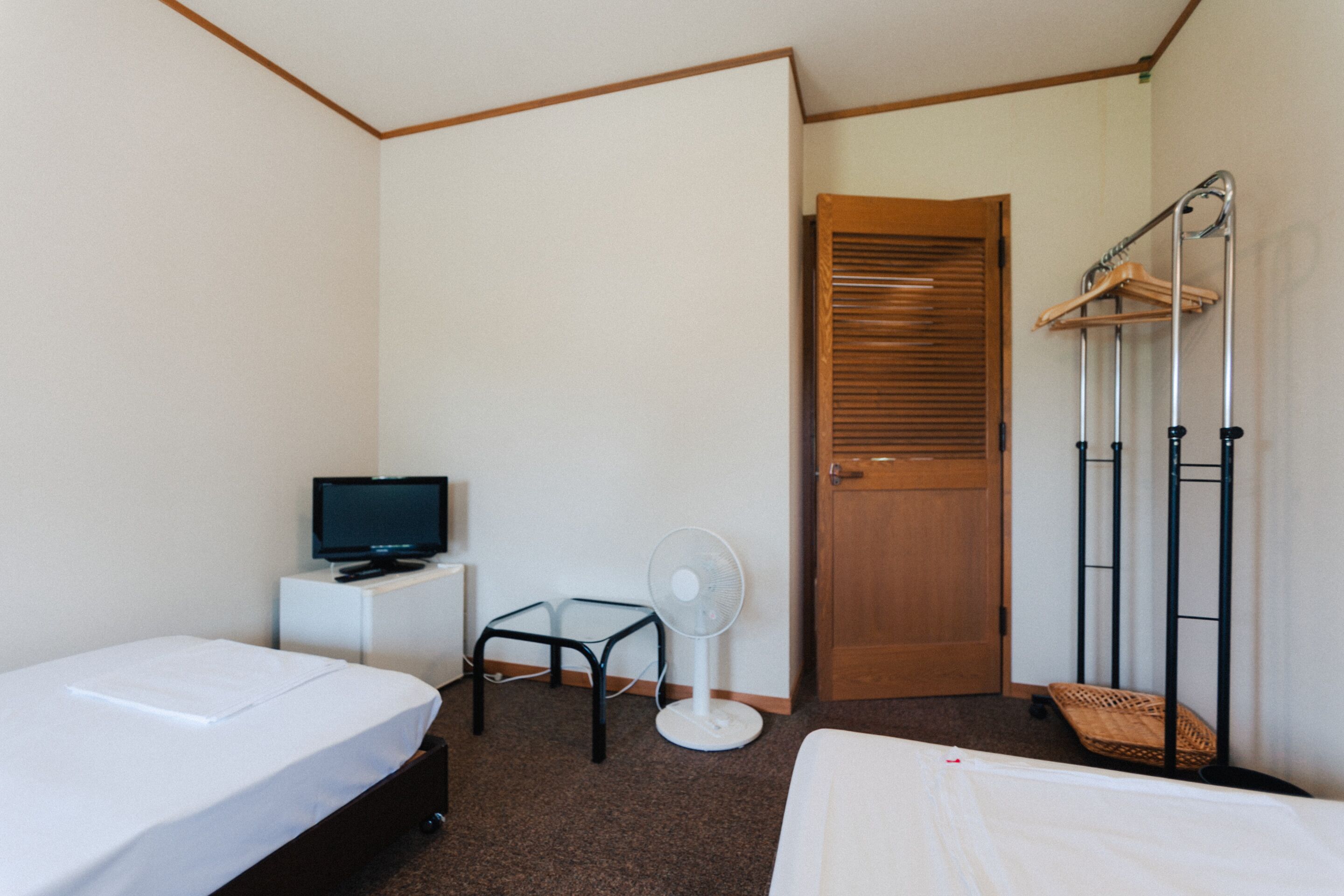 A hotel room with two beds, a television, a fan, and a wooden door.