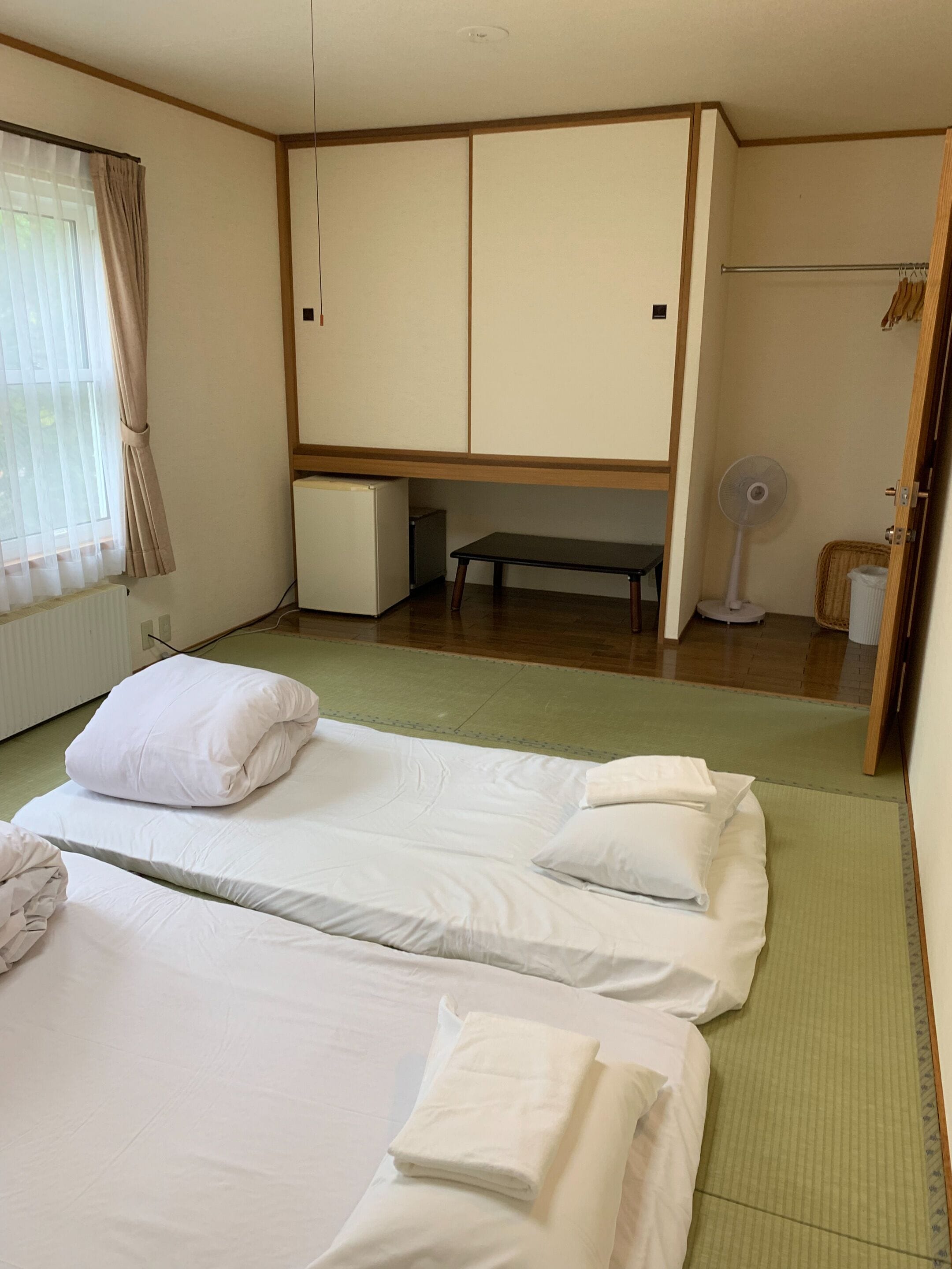 Una habitación de hotel con dos camas, un banco, un ventilador y un armario.