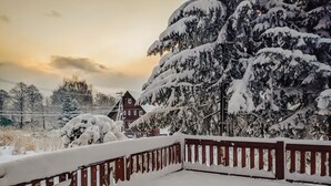 A snow-covered wooden deck with a railing, a snow-laden tree, and a red building in the background. - The Niseko Ski Lodge - Higashiyama (Niseko)