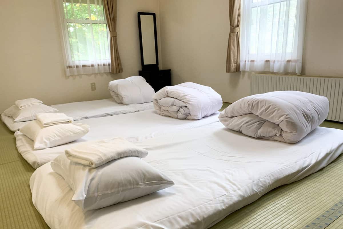 A large bed with multiple pillows and a folded blanket, a standing mirror, and a radiator.