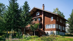 A two-story wooden house with a balcony, surrounded by trees and a garden. - The Niseko Ski Lodge - Higashiyama (Niseko)