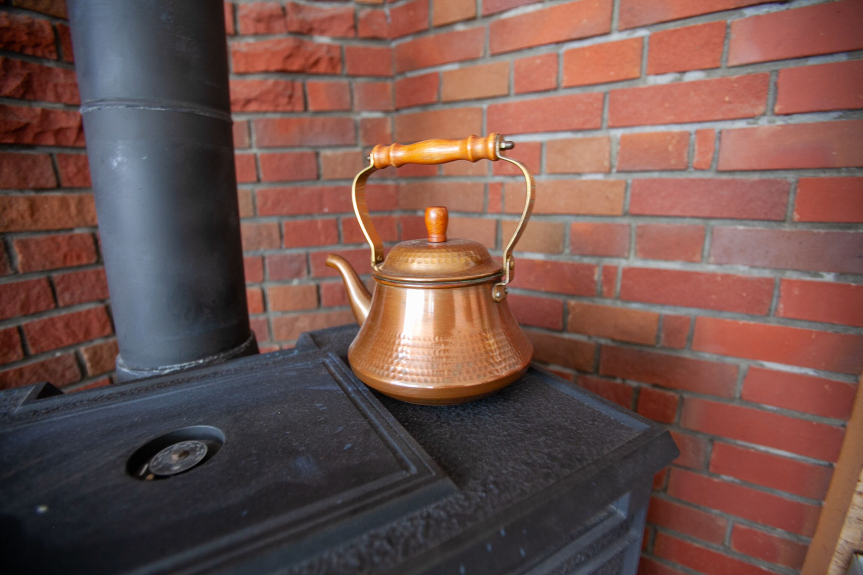 A copper kettle on a stove with a brick wall background.