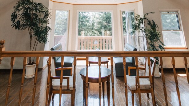 A spacious room with a sloped ceiling, wooden beams, a ceiling fan, and large windows offering views of the outdoors. - The Niseko Ski Lodge - Higashiyama (Niseko)