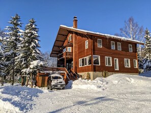 A two-story wooden cabin with a covered porch and a car parked in front.