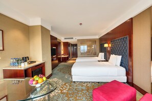 A hotel room with a bed, a desk with a fruit bowl, a red chair, and a view of the hallway. - Holiday Inn Dhaka City Centre by IHG (Dhaka)