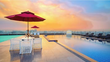 Una piscina en la azotea con sillones y sombrillas, y una vista despejada del horizonte urbano, además de un suelo de baldosas.