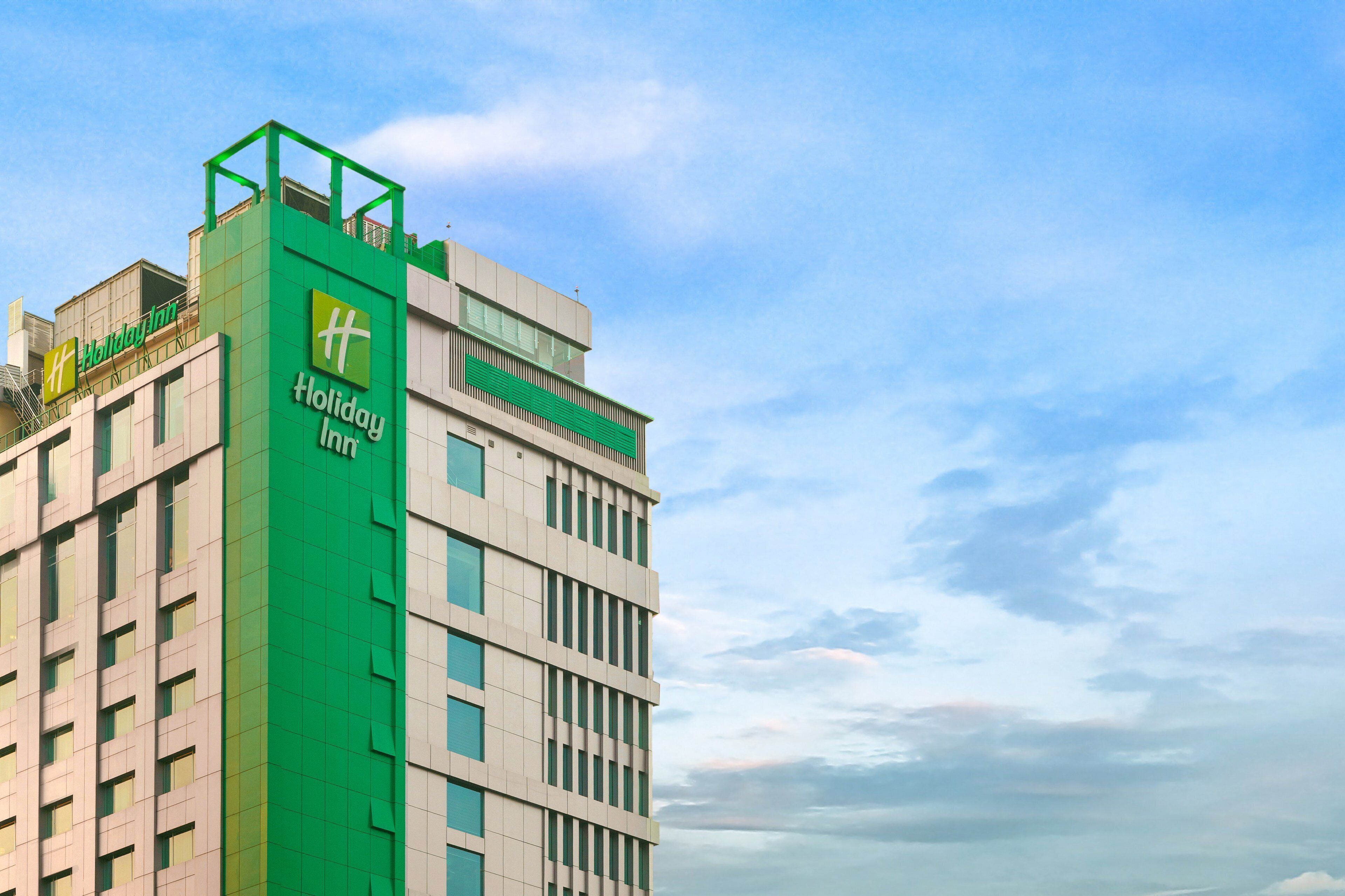 A multi-story Holiday Inn hotel with a prominent green facade and a clear sky in the background.