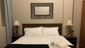 A neatly made bed with white linens, a black throw blanket, and folded towels on a wooden headboard. There are two bedside tables with lamps and decorative items. A mirror is mounted on the wall above the bed. - Boutique apartment in the heart of the Adelaide CBD (Adelaide)