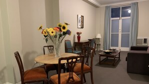 A dining area with a round table, chairs, and a vase of sunflowers. There is a sofa and a lamp in the background. - Boutique apartment in the heart of the Adelaide CBD (Adelaide)
