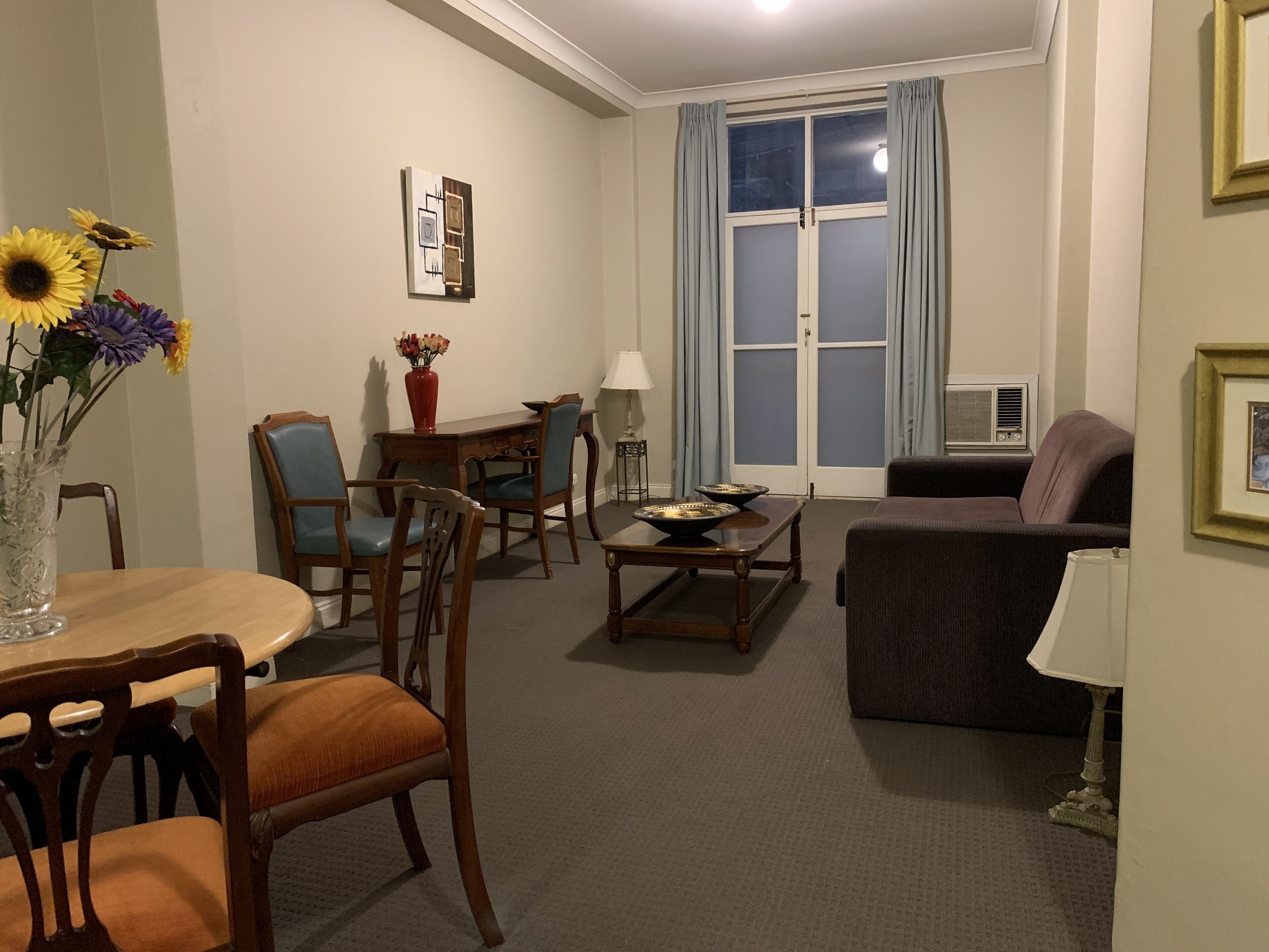 A living room with a dining table, chairs, a sofa, a coffee table, and a window with curtains.