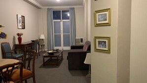 A living room with a sofa, chairs, a coffee table, and a dining table with chairs. There are framed pictures on the wall and a window with curtains. - Boutique apartment in the heart of the Adelaide CBD (Adelaide)