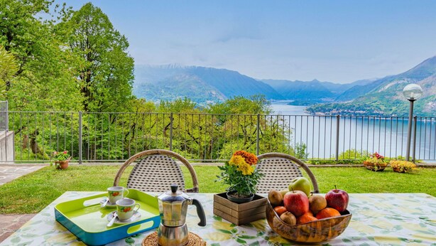 A table set outdoors with a view of a lake and mountains, a coffee pot, a fruit bowl, and a tray with cups and saucers. - Cosy apartment in villa for 4 people with WIFI, TV, terrace and pets allowed (Perledo)