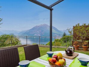Mesa posta com frutas e um bule, com vista para um lago e montanhas.