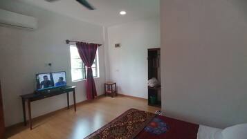 A living room with a ceiling fan, a television on a stand, a window with curtains, a small wooden table, a patterned rug, and a green trash bin.