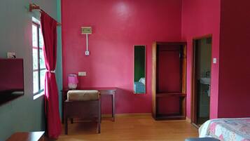 Habitación con cama, escritorio y silla. Se observa una ventana con cortinas, un espejo y una puerta que da al baño.