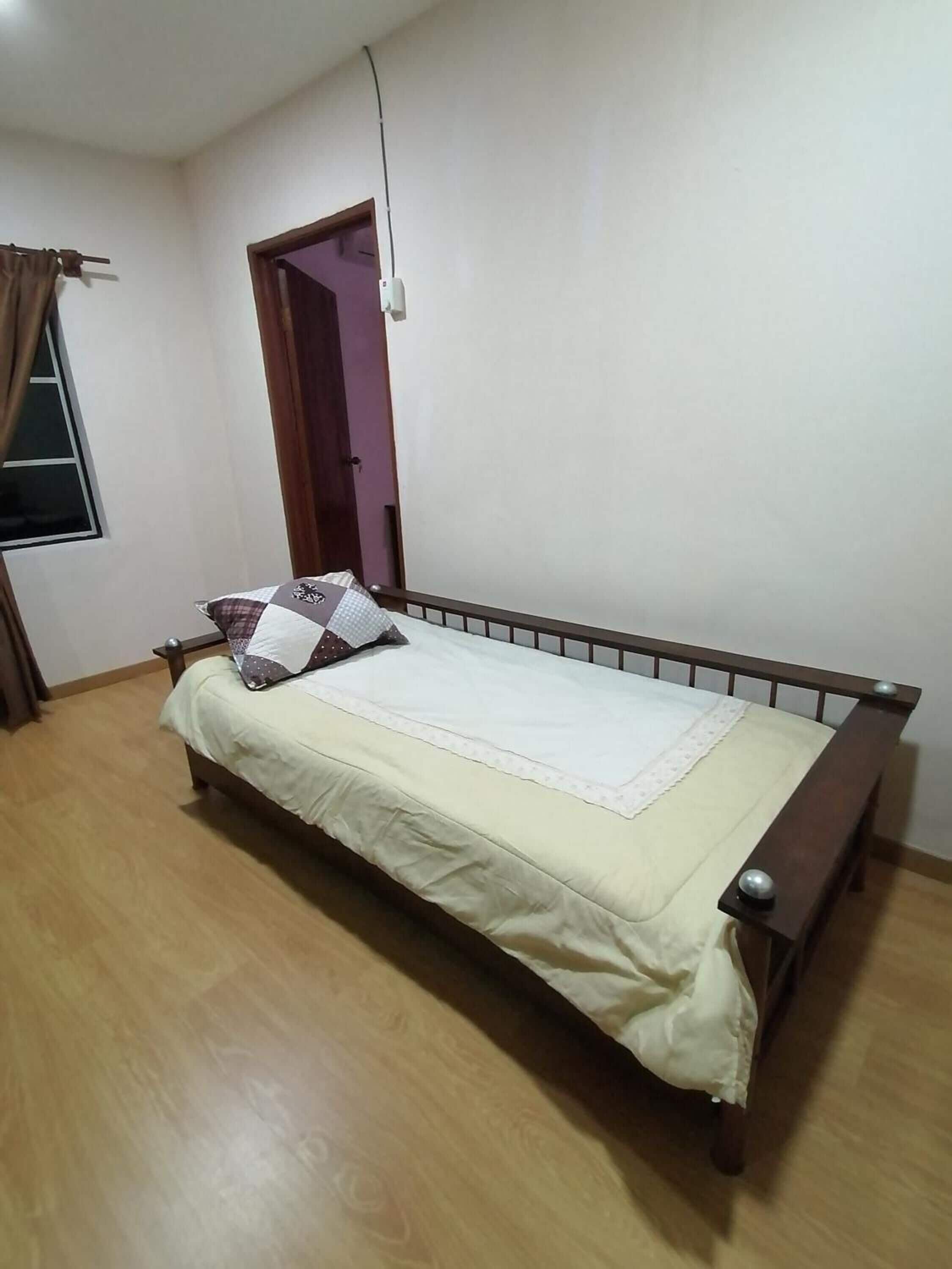 A single bed with a wooden frame and a white mattress in a room with wooden flooring and a plain white wall.