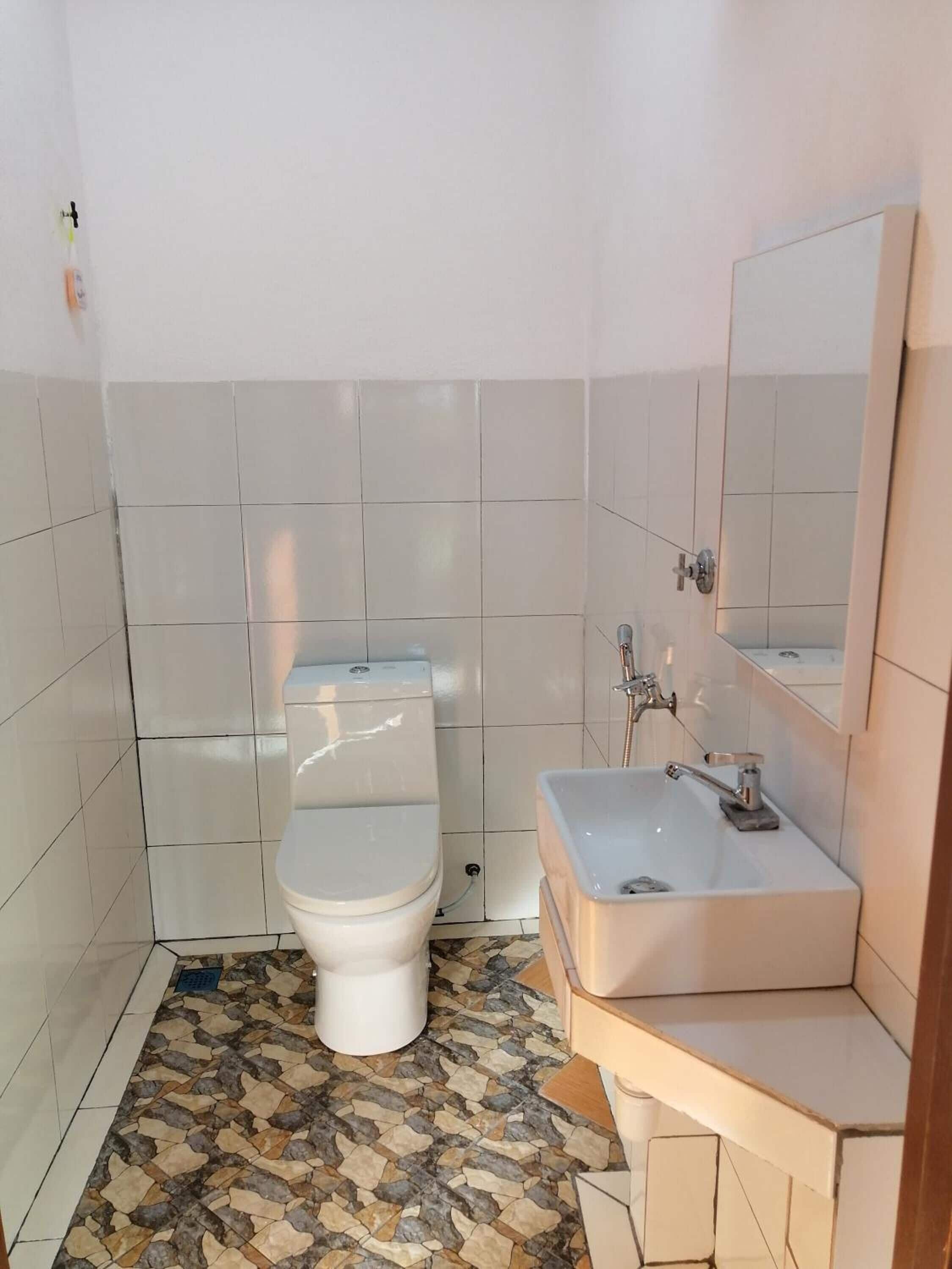 Un baño pequeño con inodoro, lavabo y espejo. El piso tiene un diseño de baldosas estampado.