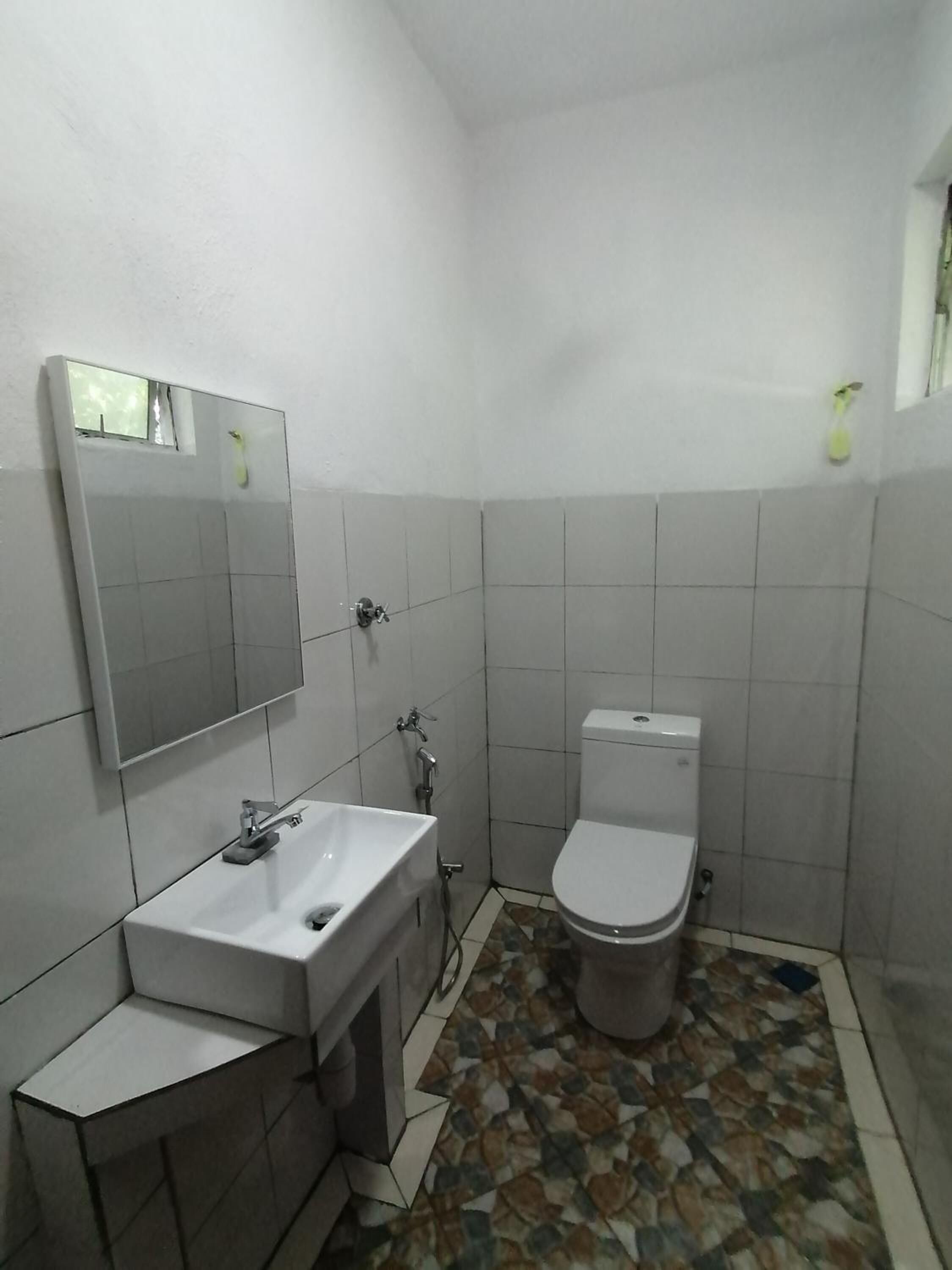 Un baño pequeño con un lavamanos blanco, un inodoro y un espejo. El piso presenta un diseño de baldosas con motivos.