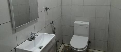 Un baño pequeño con un lavamanos blanco, un inodoro y un espejo. El piso presenta un diseño de baldosas con motivos.