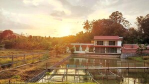 A building with a red roof and white walls, situated next to a body of water with a wooden walkway. - Guesthouse Beluru (Kuala Kangsar)
