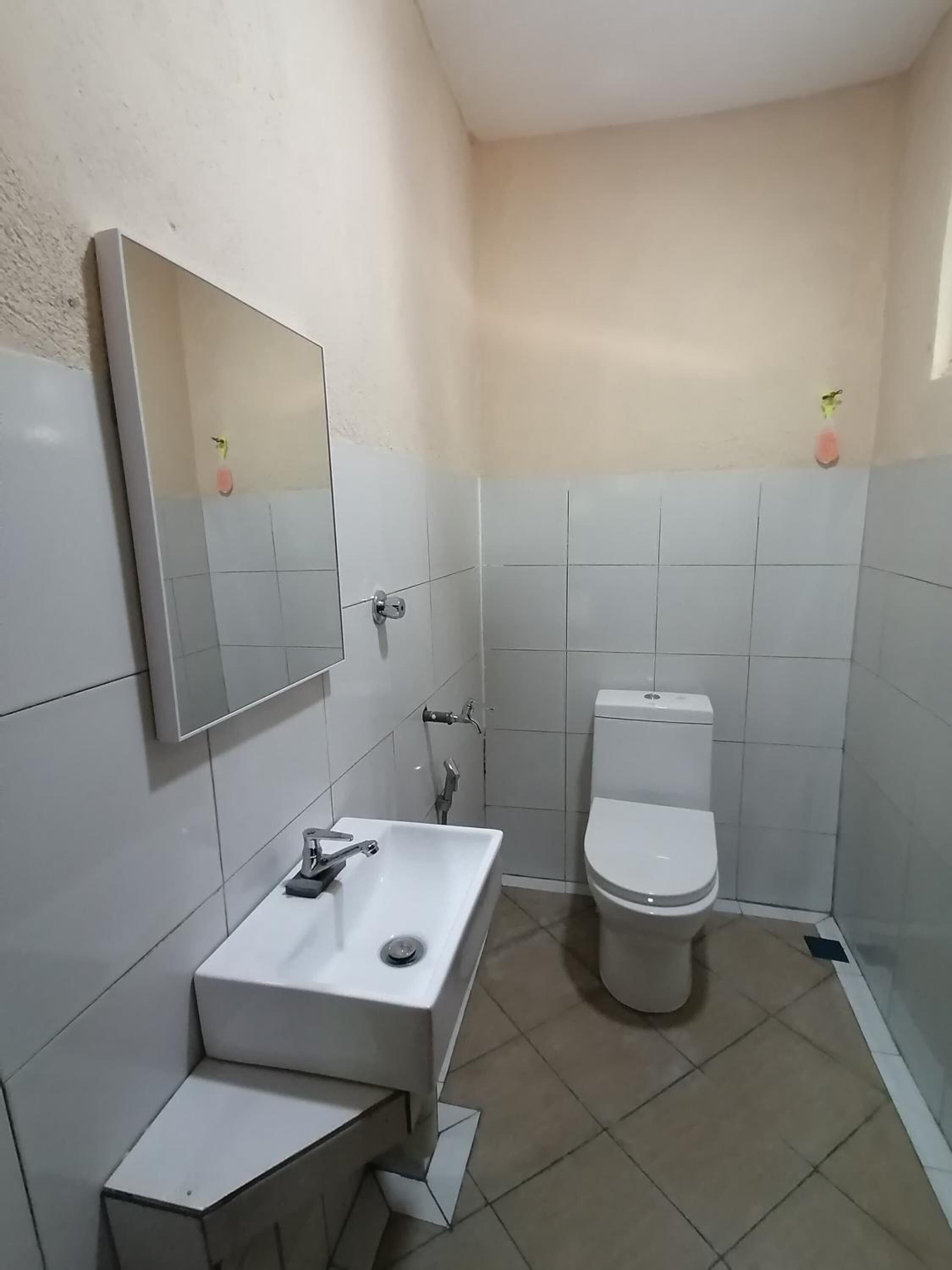Casa de banho com lavatório branco, espelho e sanita.