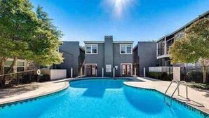 A swimming pool surrounded by modern buildings with a clear sky. - Stylish Condo near SMU, NorthPark & Greenville Ave with Pool (Dallas)