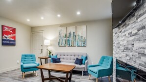 A modern living room with a grey sofa, two teal armchairs, a wooden coffee table, and a stone accent wall. - Stylish Condo near SMU, NorthPark & Greenville Ave with Pool (Dallas)