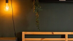 Quarto com cabeceira de madeira, planta pendente, mesa de cabeceira e prateleira com um quadro emoldurado.