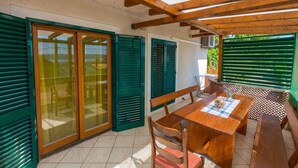 A covered patio with a wooden table and chairs, green shutters, and a view of the outdoors. - Holiday home mit Klimaanlage und Balkon (Crikvenica)