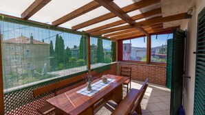A covered patio with a wooden table and benches, a view through a mesh screen, and a brick wall. - Holiday home mit Klimaanlage und Balkon (Crikvenica)
