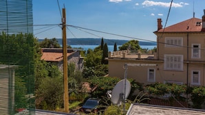 A residential area with a house featuring a satellite dish, a car parked in front, and a view of the sea in the background. - Holiday home mit Klimaanlage und Balkon (Crikvenica)