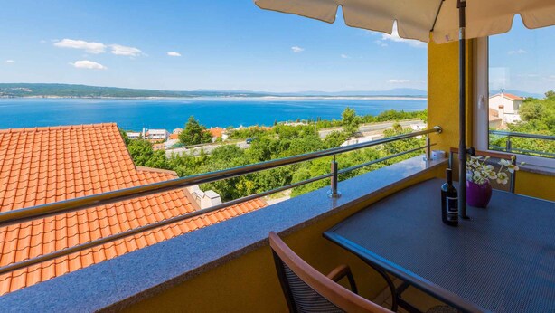 Un balcon avec vue sur la mer, une table avec une bouteille et des fleurs.
