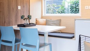 Una cocina moderna con una pared decorativa de madera, encimera blanca, ventana con vistas a zonas verdes y sillas azules.