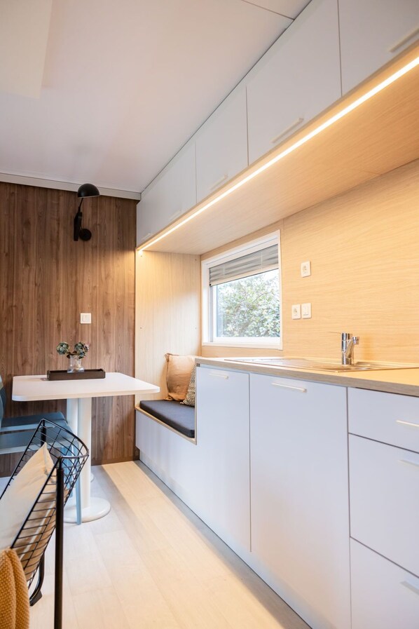 A modern kitchen with white cabinets, a wooden accent wall, a window with blinds, and a built-in bench with cushions.