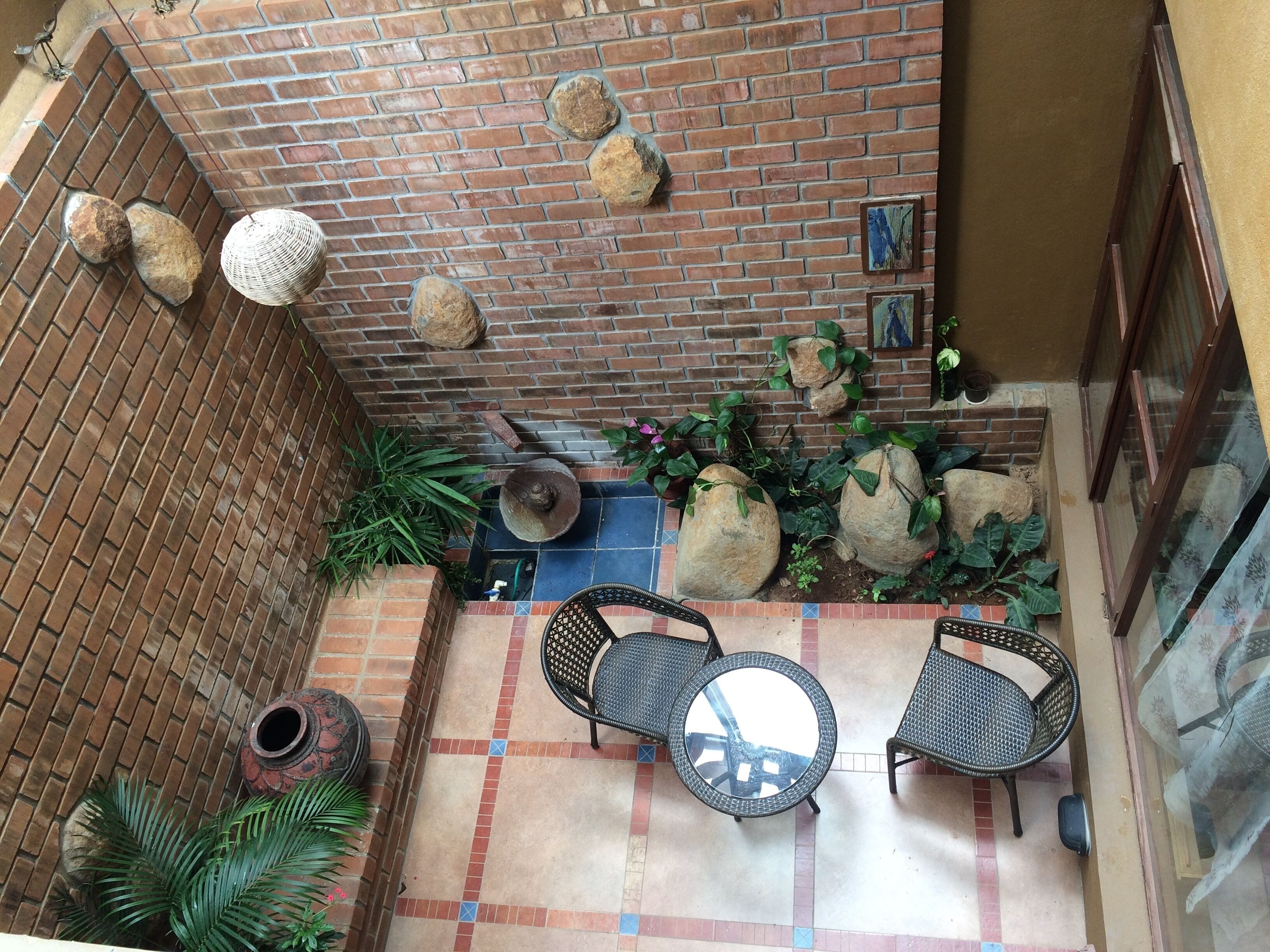 A patio with a brick wall, two round tables, and chairs, surrounded by potted plants and rocks.