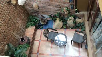 A patio with a brick wall, two round tables, and chairs, surrounded by potted plants and rocks.
