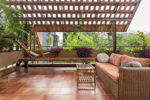 A covered patio with a wicker sofa, a bench, and a hanging chair.