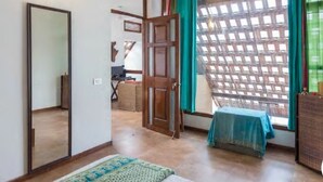 A room with a wooden door, a mirror, a window with a lattice, and a small table with a blue tablecloth.