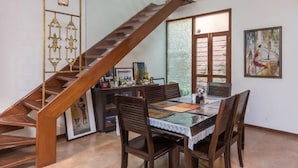 A dining area with a wooden staircase, a table with chairs, and a view through large windows.