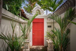 A red door with a white decorative archway, surrounded by lush green plants and a white wall. - View Talay Villas Pattaya (Pattaya)