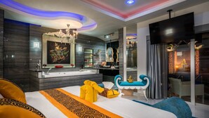 A modern hotel room with a large bed, a chandelier, a television, and a bathroom with a mirror and sink. - View Talay Villas Pattaya (Pattaya)