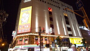 Un bâtiment bien éclairé, avec une enseigne 7-Eleven bien visible, une grande publicité lumineuse et un magasin 7-Eleven situé au rez-de-chaussée.