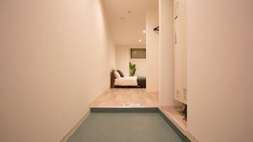 A narrow hallway with a green carpet leading to a room with a bed and a plant.