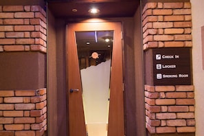 Entrada de hotel con pared de ladrillo, puerta de madera y señalización que indica recepción, consigna y sala para fumadores.