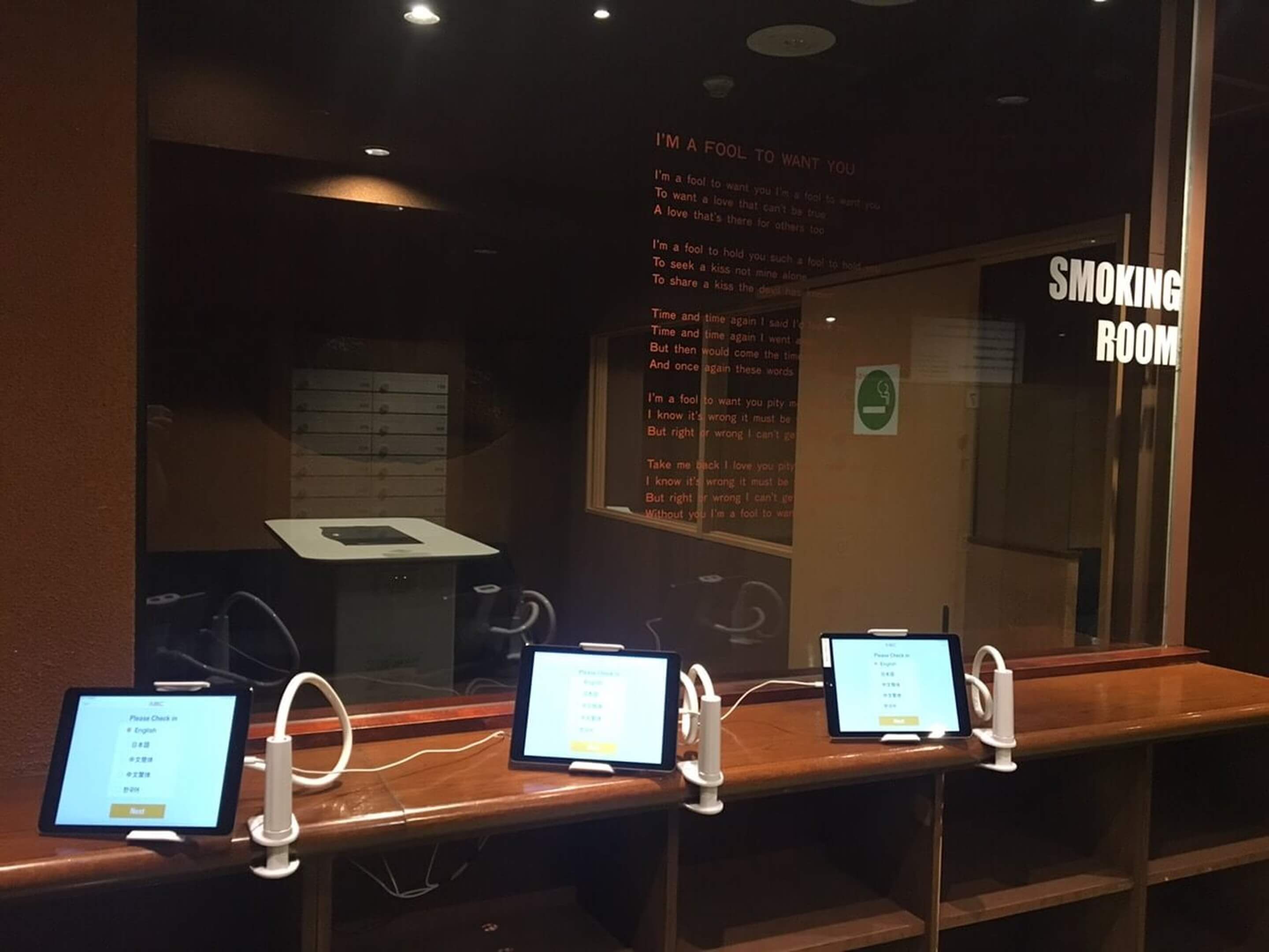 A smoking room with a menu board displaying a list of items. There are three digital screens on a counter, each displaying a menu.